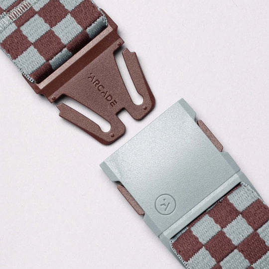 A close-up of the Arcade Belts Check: a performance stretch belt with brown and light gray checkered squares, featuring a brown plastic buckle labeled ARCADE and a matching light gray clasp—built for movement.