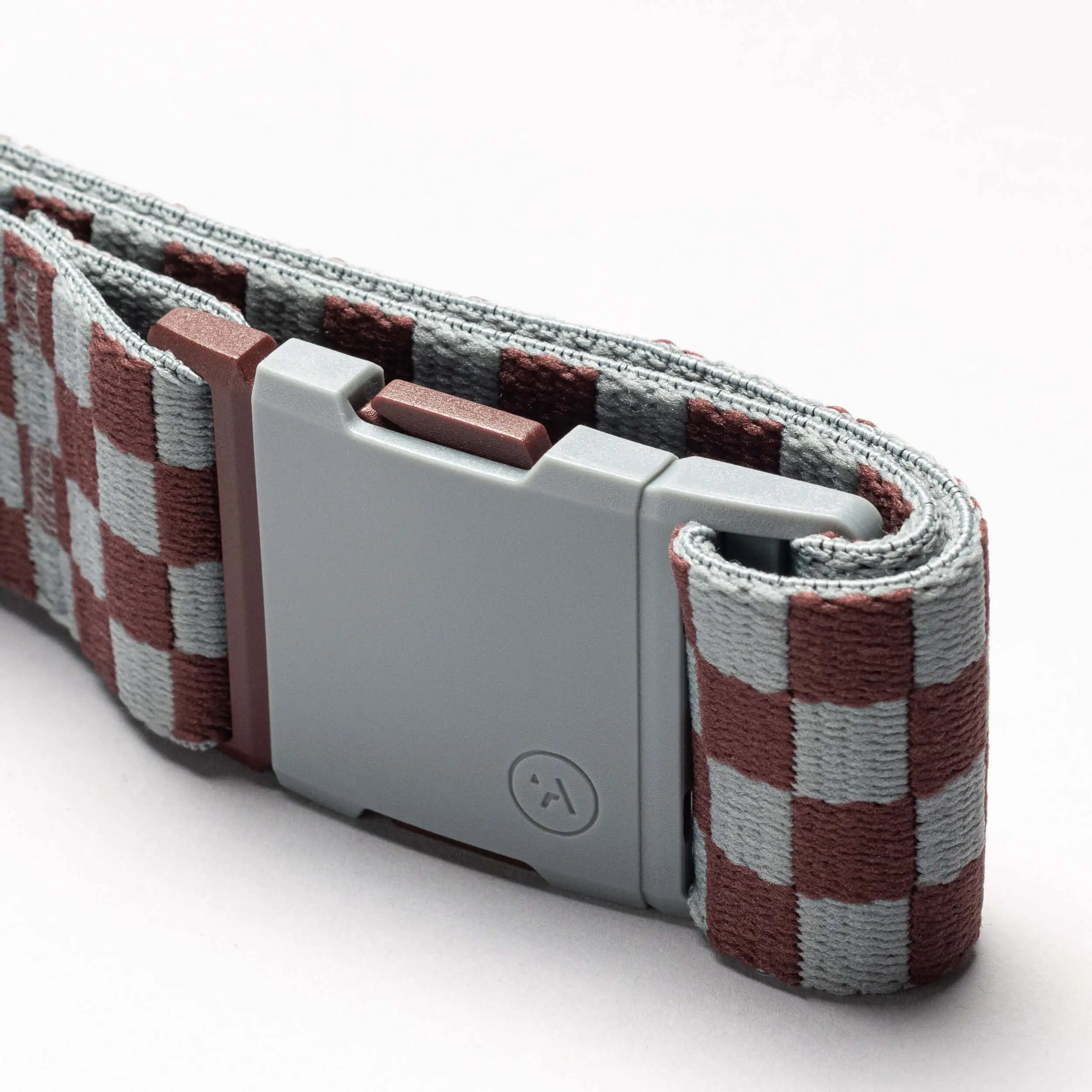 A close-up of the Arcade Belts Check belt, featuring a gray plastic buckle and a brown and light gray checkered performance stretch strap, showcased against a plain white background.