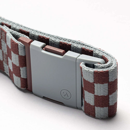 A close-up of the Arcade Belts Check belt, featuring a gray plastic buckle and a brown and light gray checkered performance stretch strap, showcased against a plain white background.