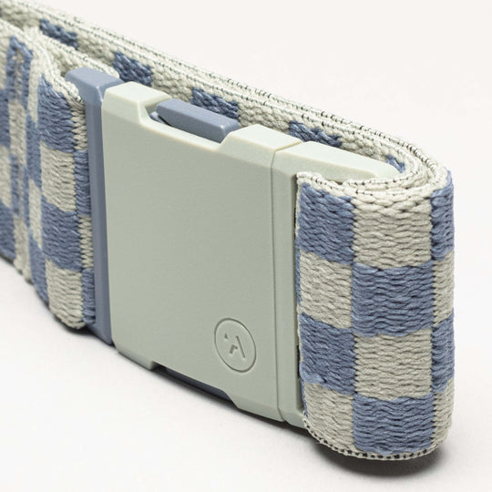 A close-up of the Arcade Belts Check, a fabric belt with a blue and gray checkerboard pattern, matte light gray rectangular buckle, and performance stretch for comfort, shown against a plain light background.