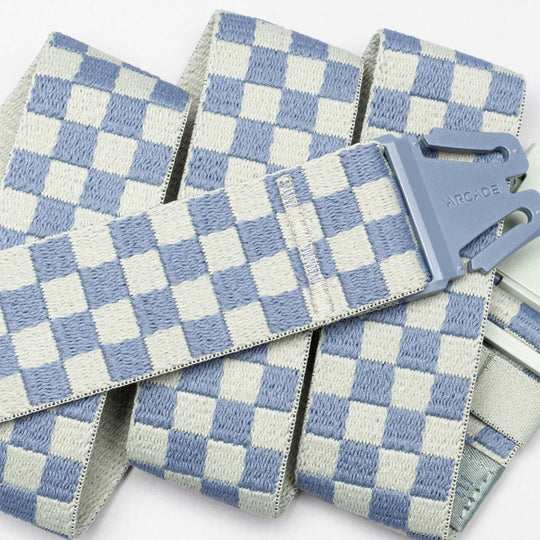 A close-up of the Arcade Belts "Check" shows its blue and white checkerboard pattern and gray buckle, featuring performance stretch for those who prioritize comfort in athletic wear.