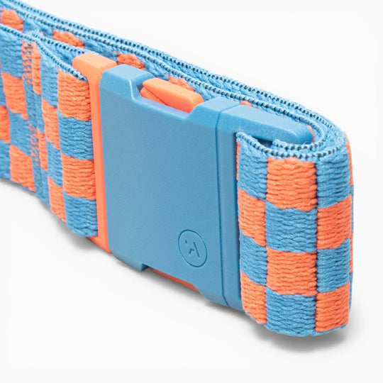 A close-up of the Arcade Belts Check, a blue and orange checkered fabric strap with a blue plastic buckle on a white background, featuring performance stretch made for movement and designed to turn heads wherever you go.