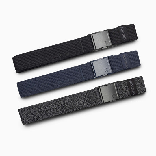 The Atlas Slim Kit by Arcade Belts includes three fabric belts—black, navy blue, and heathered gray—each with a slim, low-profile buckle labeled ARCADE, making them ideal travel companions for any adventure.