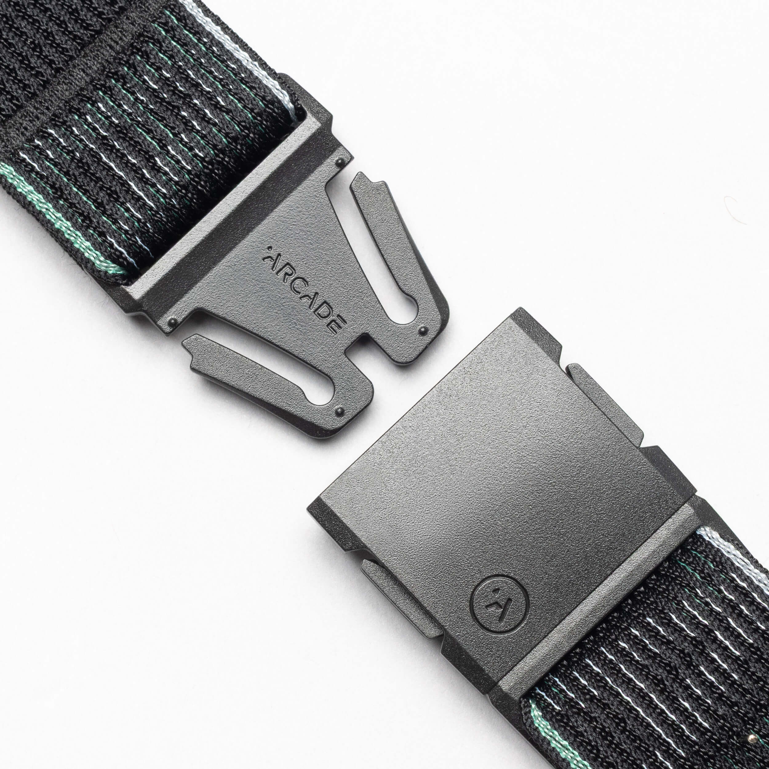 Close-up of the Arcade Belts Cubed belt in black fabric with a metal buckle, partially unclasped to reveal the brand name. Comfortable design features subtle light green accents for added style.