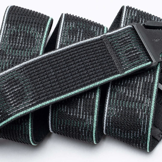 A close-up photo of the Arcade Belts Cubed—a black belt with light green edging and white stitching—folded beside a plastic buckle on a white background, showcasing its comfortable and stylish design.