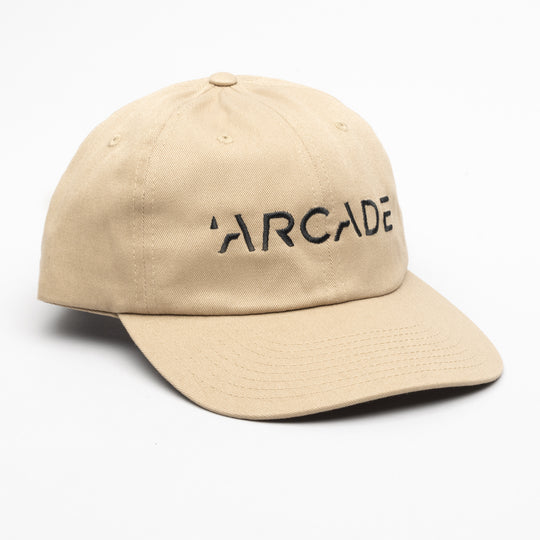 The Arcade Dad Hat by Arcade Belts is a beige baseball cap featuring “ARCADE” in black capital letters on the front, inspired by their iconic low profile belt style, shown on a white background.