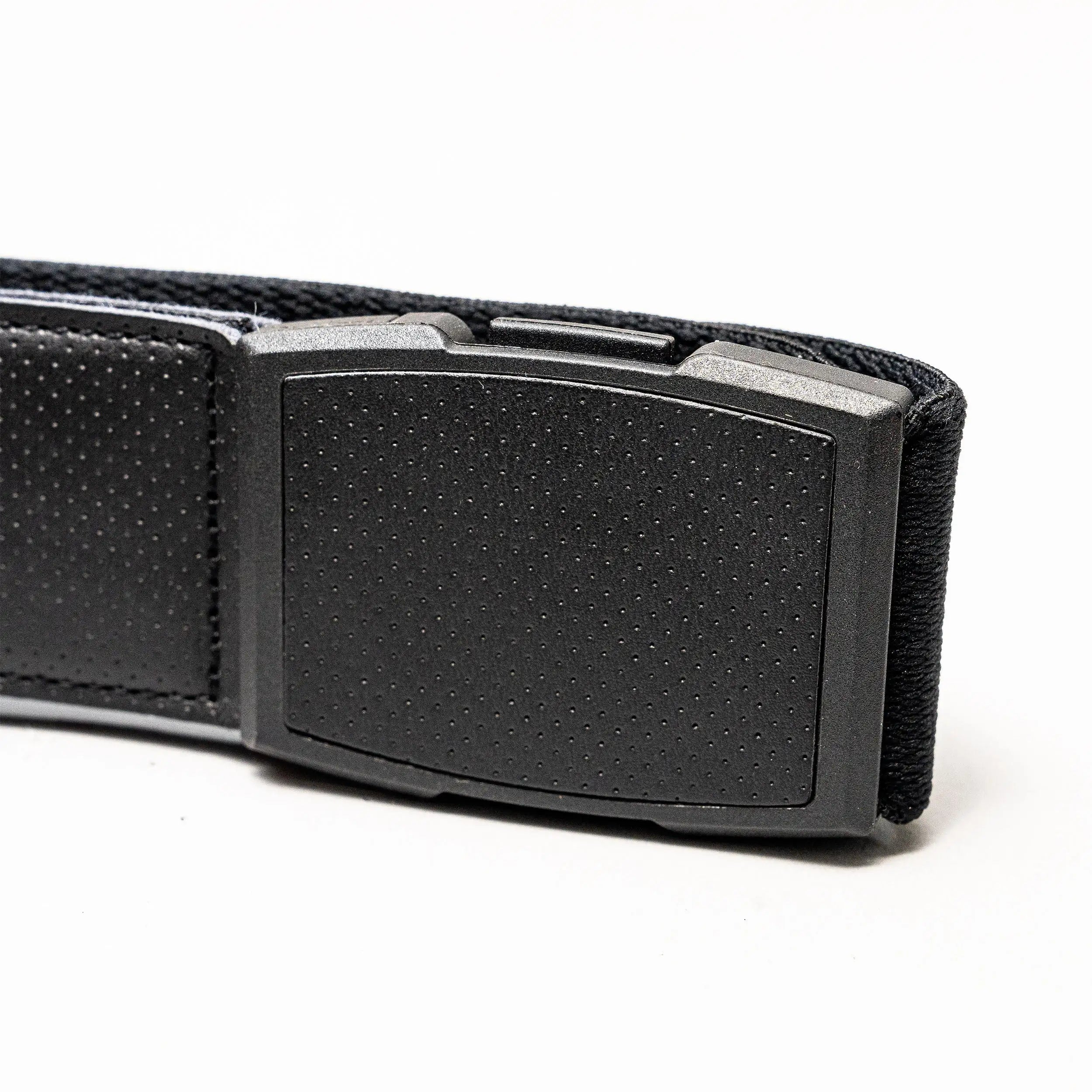 Close-up of the Elevation belt by Arcade Belts: a black, rectangular plastic buckle with a dotted pattern on a textured black stretch webbing strap combining fabric and leather, shown against a white background.