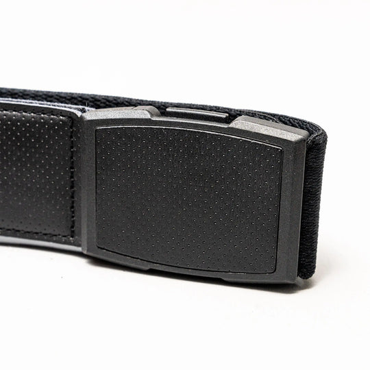 Close-up of the Elevation belt by Arcade Belts: a black, rectangular plastic buckle with a dotted pattern on a textured black stretch webbing strap combining fabric and leather, shown against a white background.
