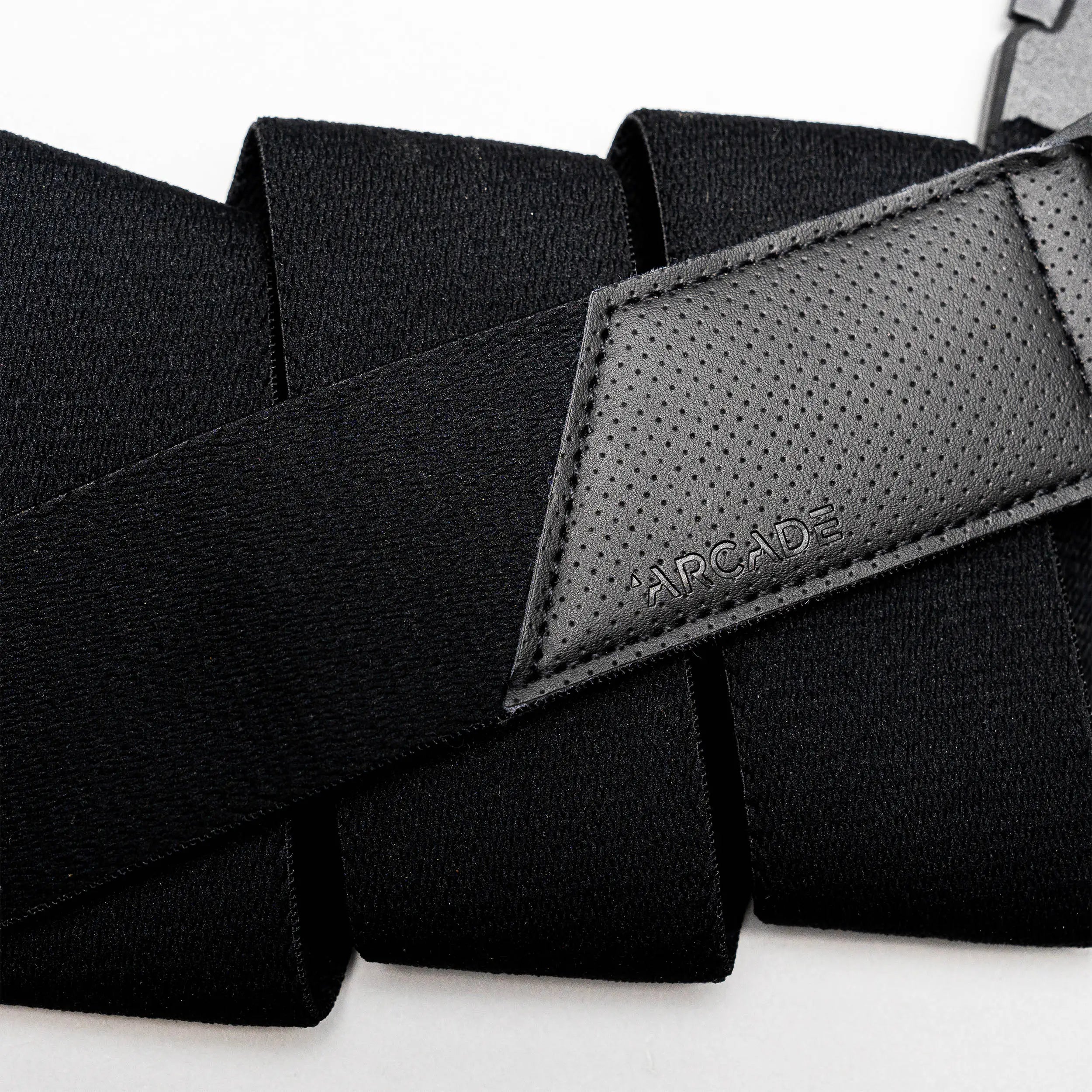 A close-up of Arcade Belts Elevation: a black travel belt with stretch webbing, a textured leather patch embossed with the logo, and a strong plastic buckle.