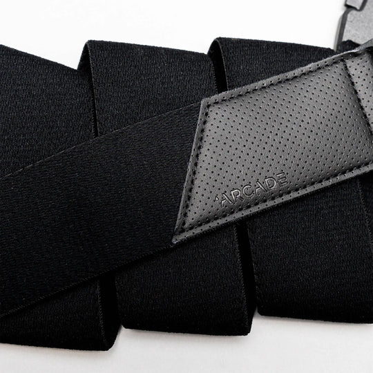 A close-up of Arcade Belts Elevation: a black travel belt with stretch webbing, a textured leather patch embossed with the logo, and a strong plastic buckle.