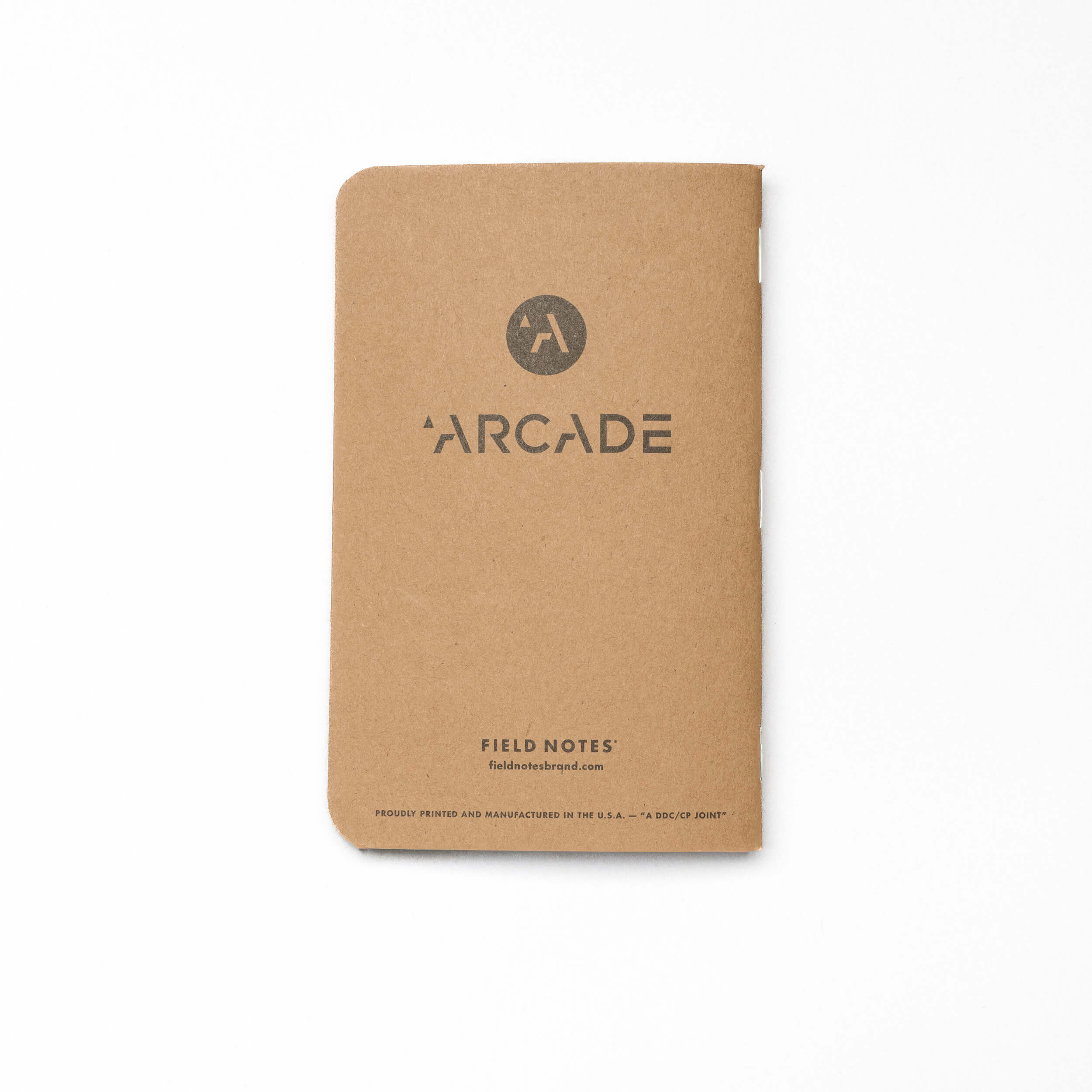 A brown, portable Field Notes notebook by Arcade Belts features a circular logo and "FIELD NOTES" plus the website on the cover. With durable construction, rounded corners, and a minimalist design, it’s ideal for on-the-go note-taking.