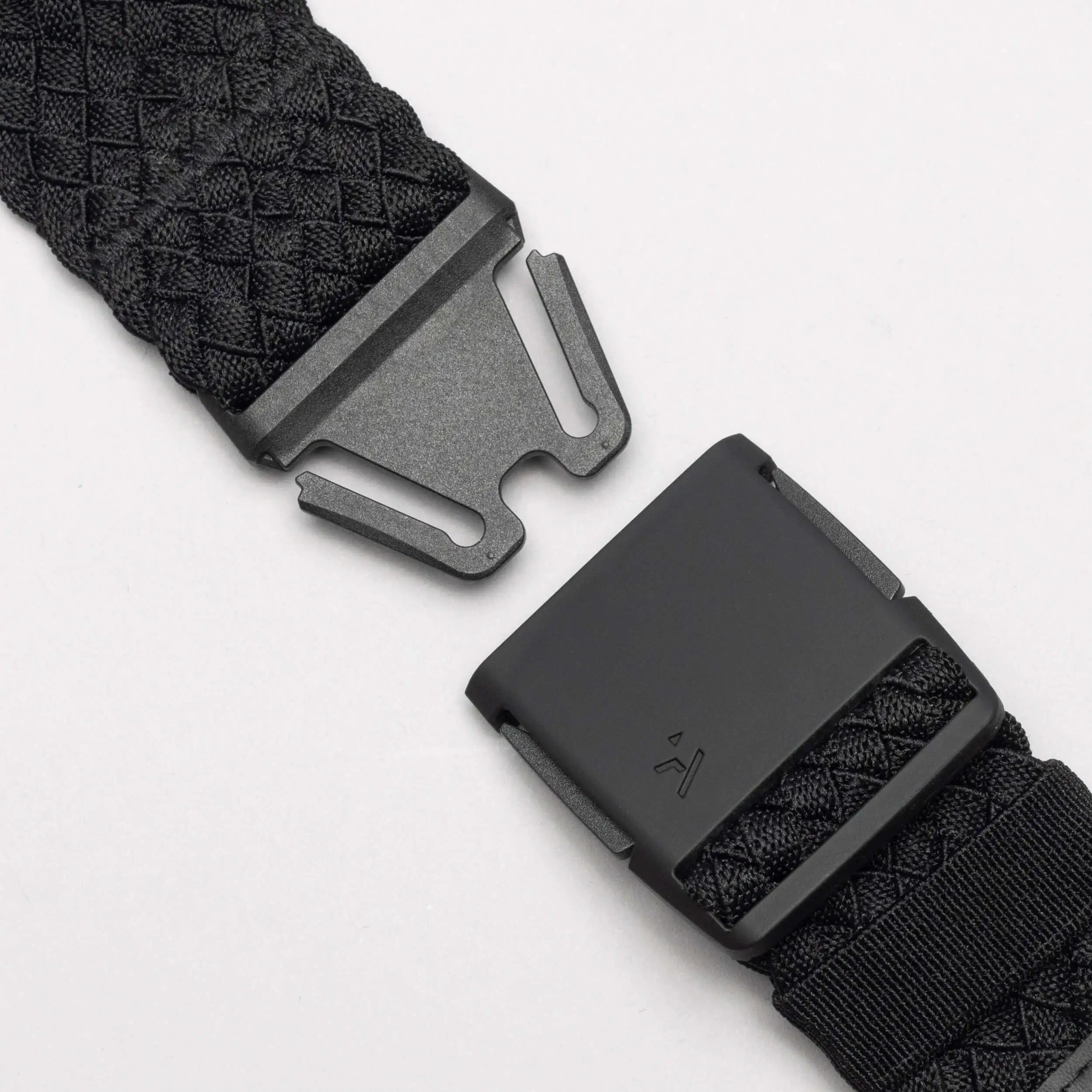 Close-up of the Arcade Belts Futureweave: a black woven belt with a matte black metal buckle, shown partially unclasped against a white background. It features a textured crisscross pattern for a comfortable fit.