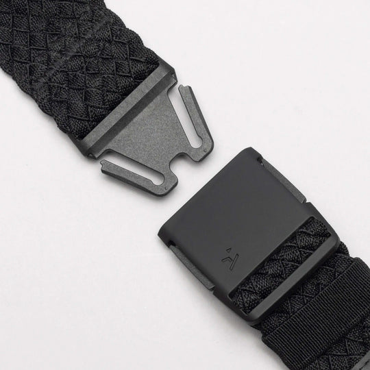 Close-up of the Arcade Belts Futureweave: a black woven belt with a matte black metal buckle, shown partially unclasped against a white background. It features a textured crisscross pattern for a comfortable fit.