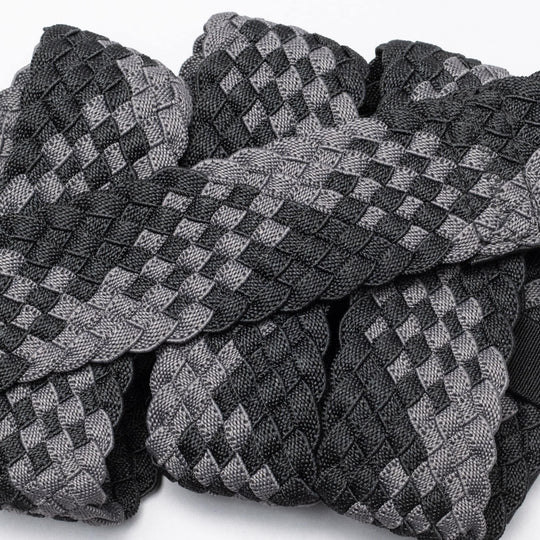 A close-up of Futureweave by Arcade Belts shows intricately woven webbing fabric strips in a black and gray checkerboard pattern, arranged in an overlapping design.