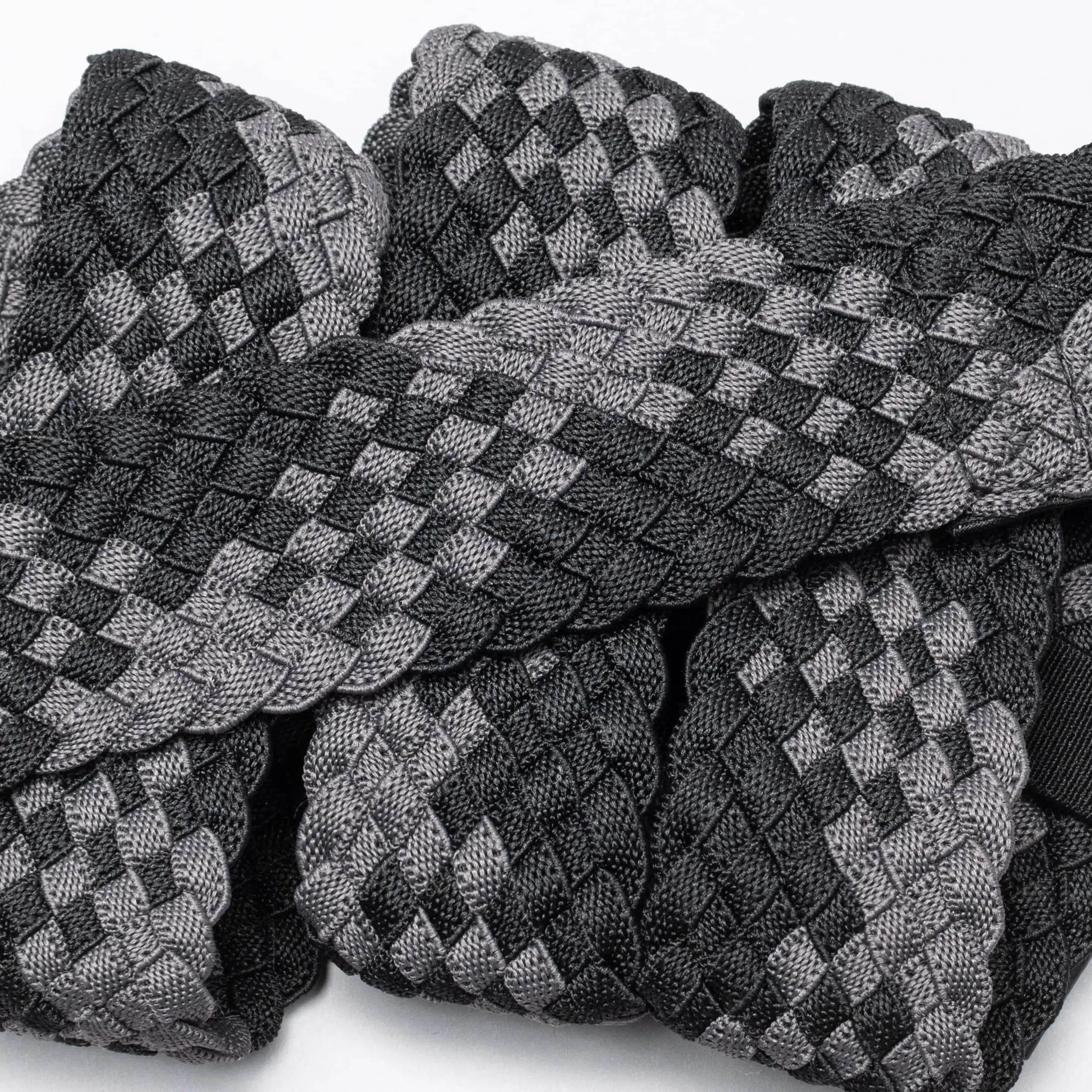 A close-up of Futureweave by Arcade Belts shows intricately woven webbing fabric strips in a black and gray checkerboard pattern, arranged in an overlapping design.
