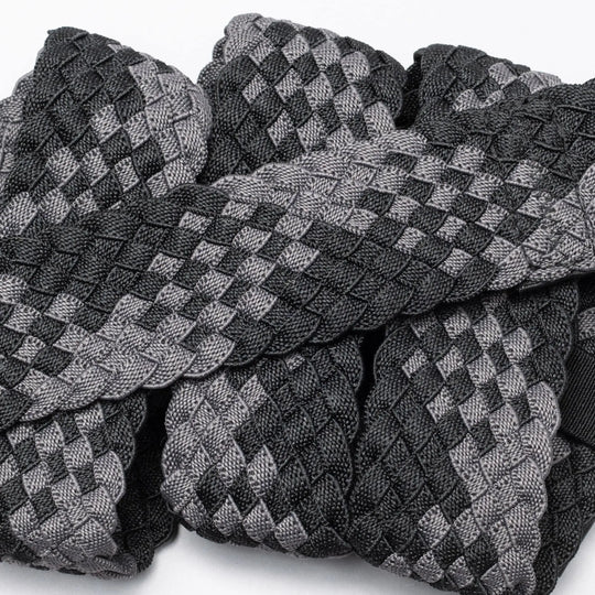 A close-up of Futureweave by Arcade Belts shows intricately woven webbing fabric strips in a black and gray checkerboard pattern, arranged in an overlapping design.