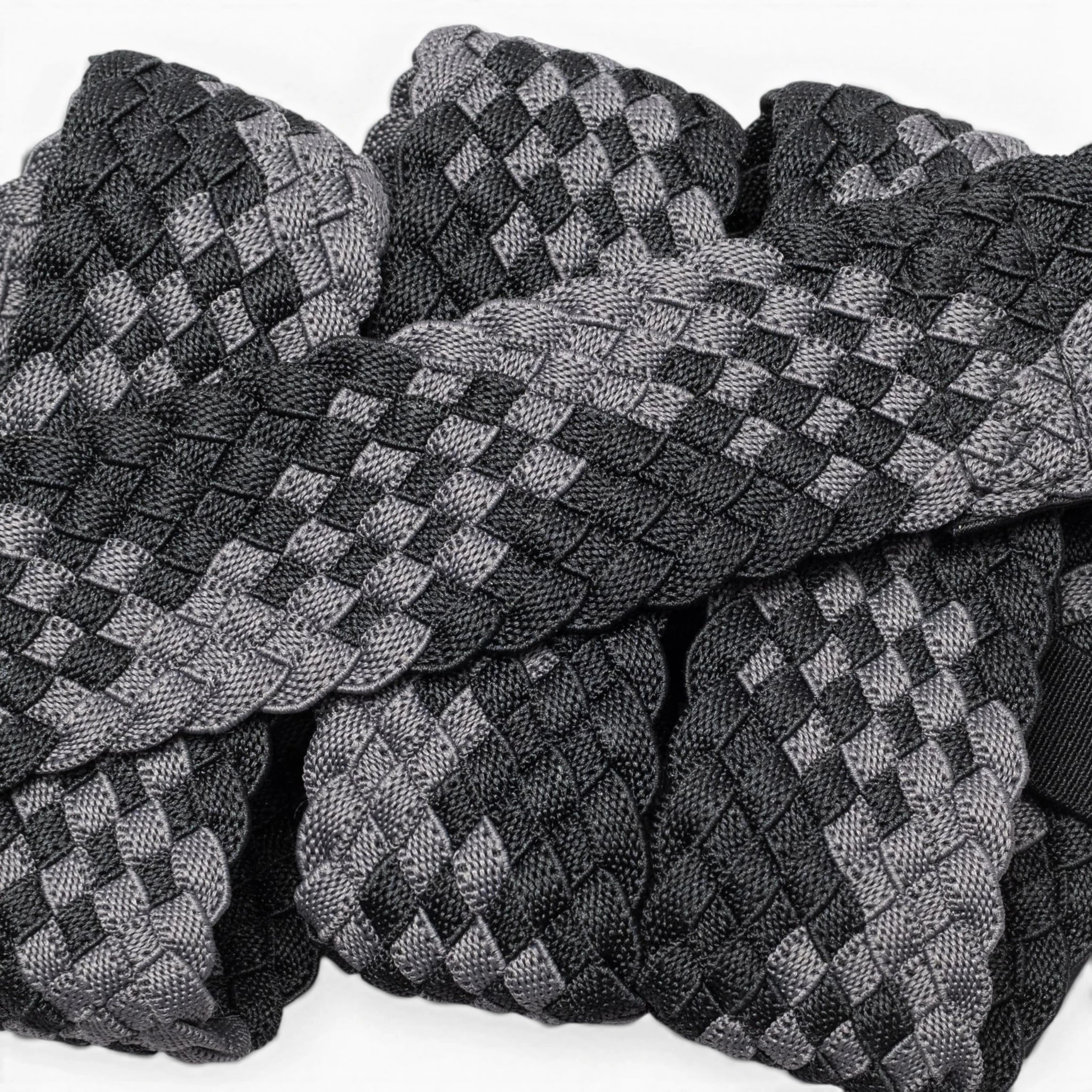 A close-up of Futureweave by Arcade Belts shows intricately woven webbing fabric strips in a black and gray checkerboard pattern, arranged in an overlapping design.