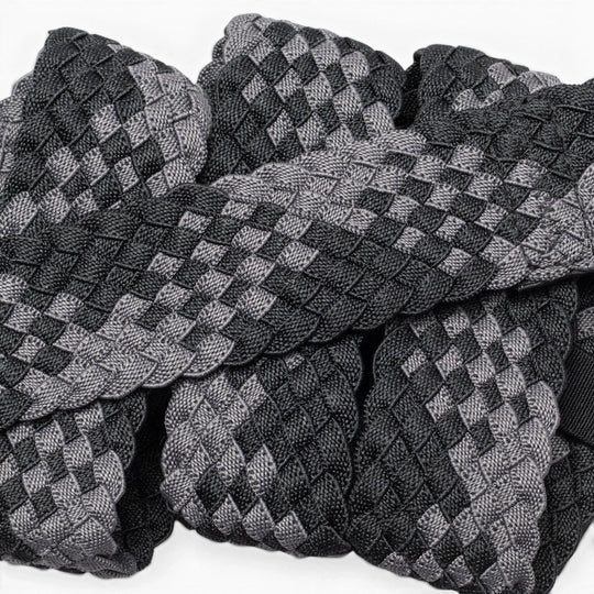 A close-up of Futureweave by Arcade Belts shows intricately woven webbing fabric strips in a black and gray checkerboard pattern, arranged in an overlapping design.