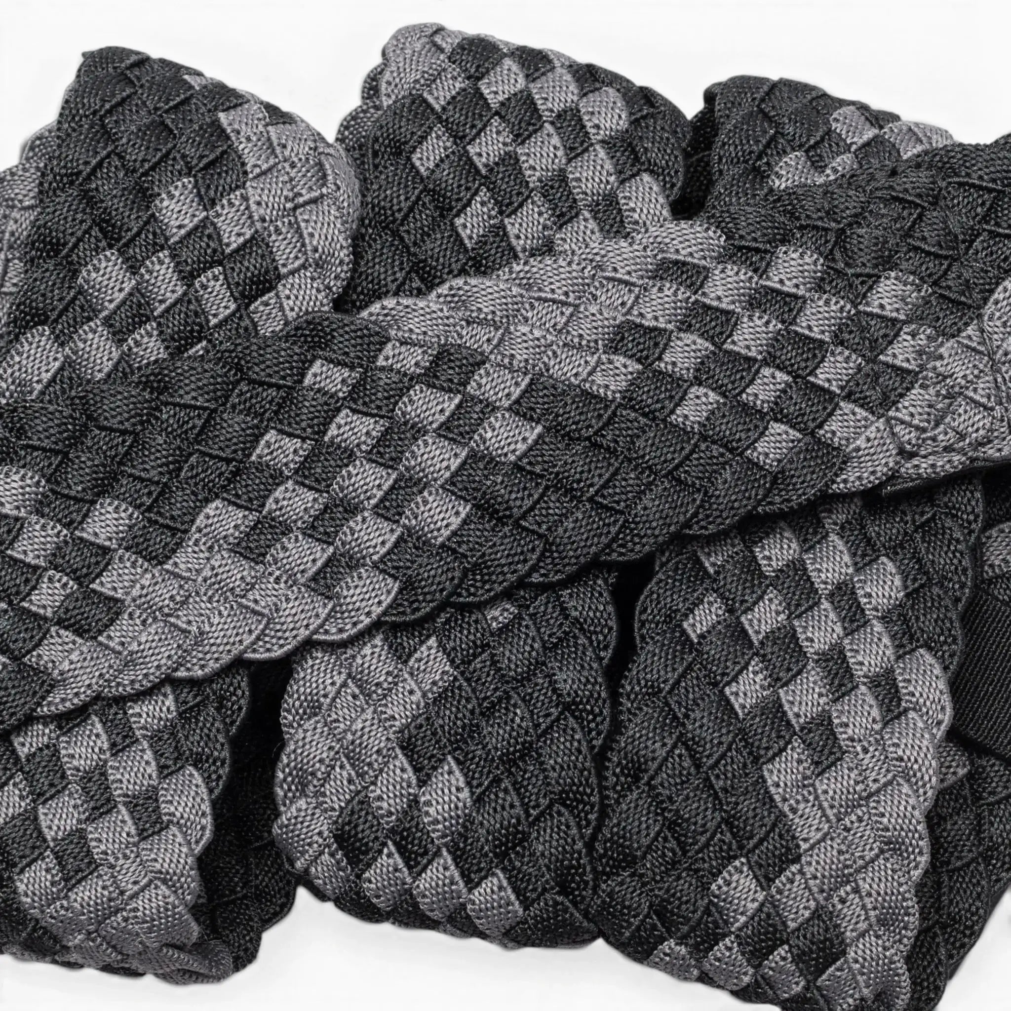 A close-up of Futureweave by Arcade Belts shows intricately woven webbing fabric strips in a black and gray checkerboard pattern, arranged in an overlapping design.