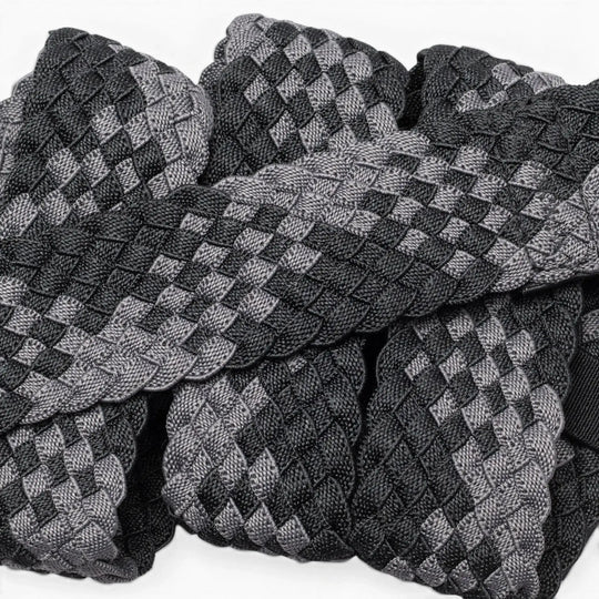 A close-up of Futureweave by Arcade Belts shows intricately woven webbing fabric strips in a black and gray checkerboard pattern, arranged in an overlapping design.