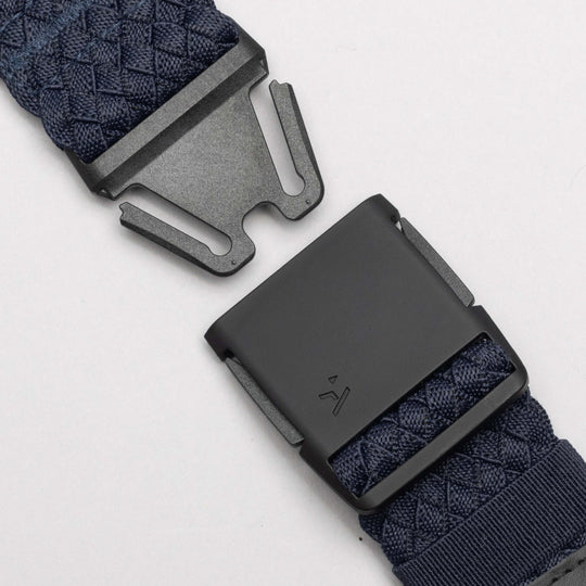 Close-up of the Arcade Belts Futureweave, a navy blue woven webbing belt with a matte black metal buckle, shown partially unfastened on a light gray background for a comfortable, lightweight fit.