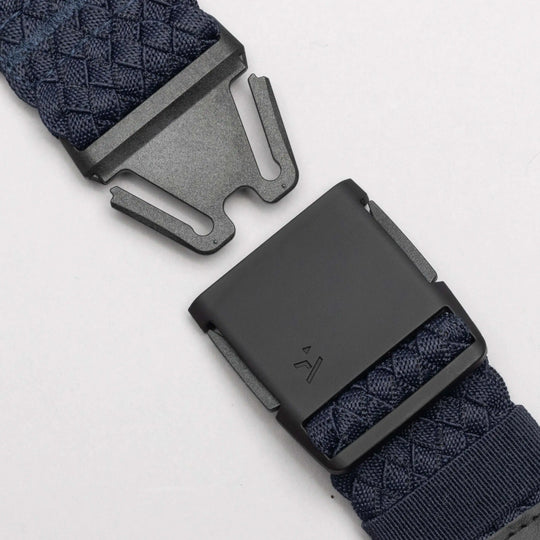 Close-up of the Arcade Belts Futureweave, a navy blue woven webbing belt with a matte black metal buckle, shown partially unfastened on a light gray background for a comfortable, lightweight fit.