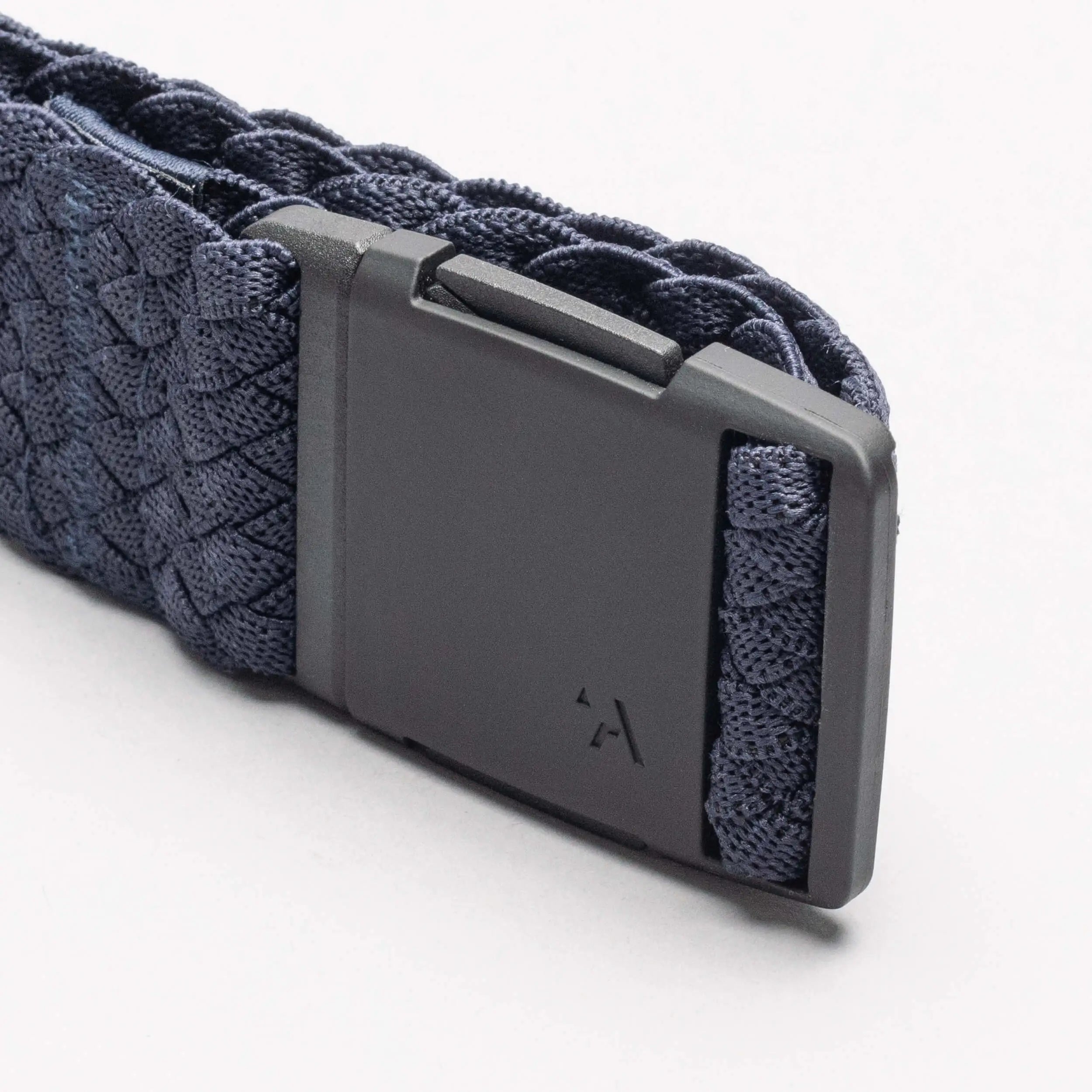 Close-up of a dark blue Arcade Belts Futureweave elastic stretch belt with a matte black plastic buckle, featuring a small, subtle logo on the buckle, shown on a white background.
