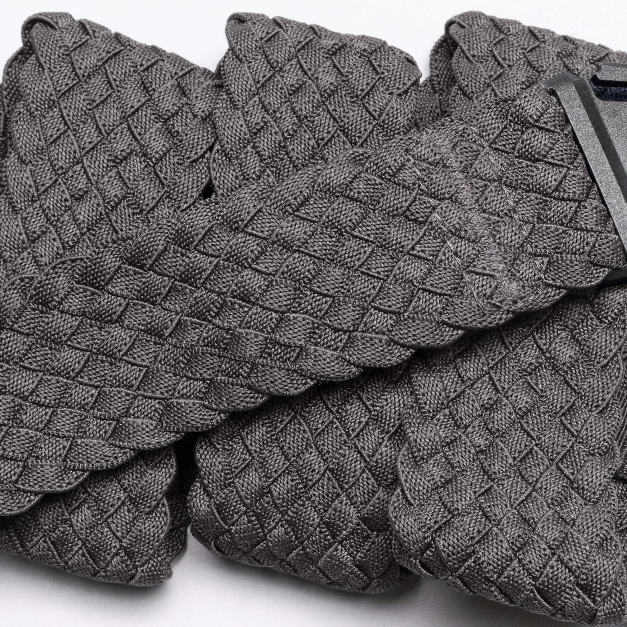 A close-up of Futureweave by Arcade Belts shows its textured gray basketweave fabric, featuring folded sections and a partially visible clothing tag in the top right corner.
