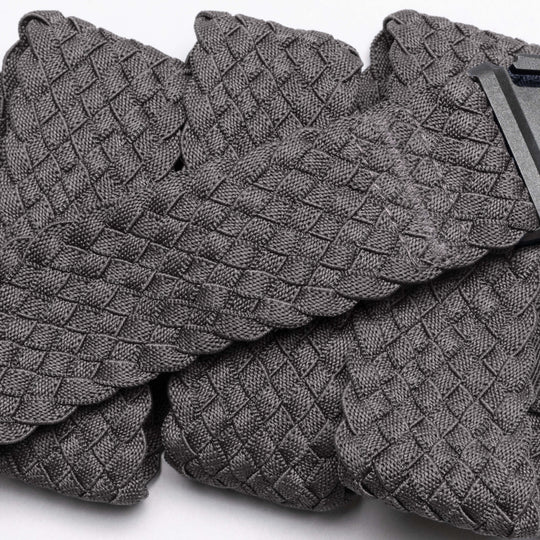 A close-up of Futureweave by Arcade Belts shows its textured gray basketweave fabric, featuring folded sections and a partially visible clothing tag in the top right corner.
