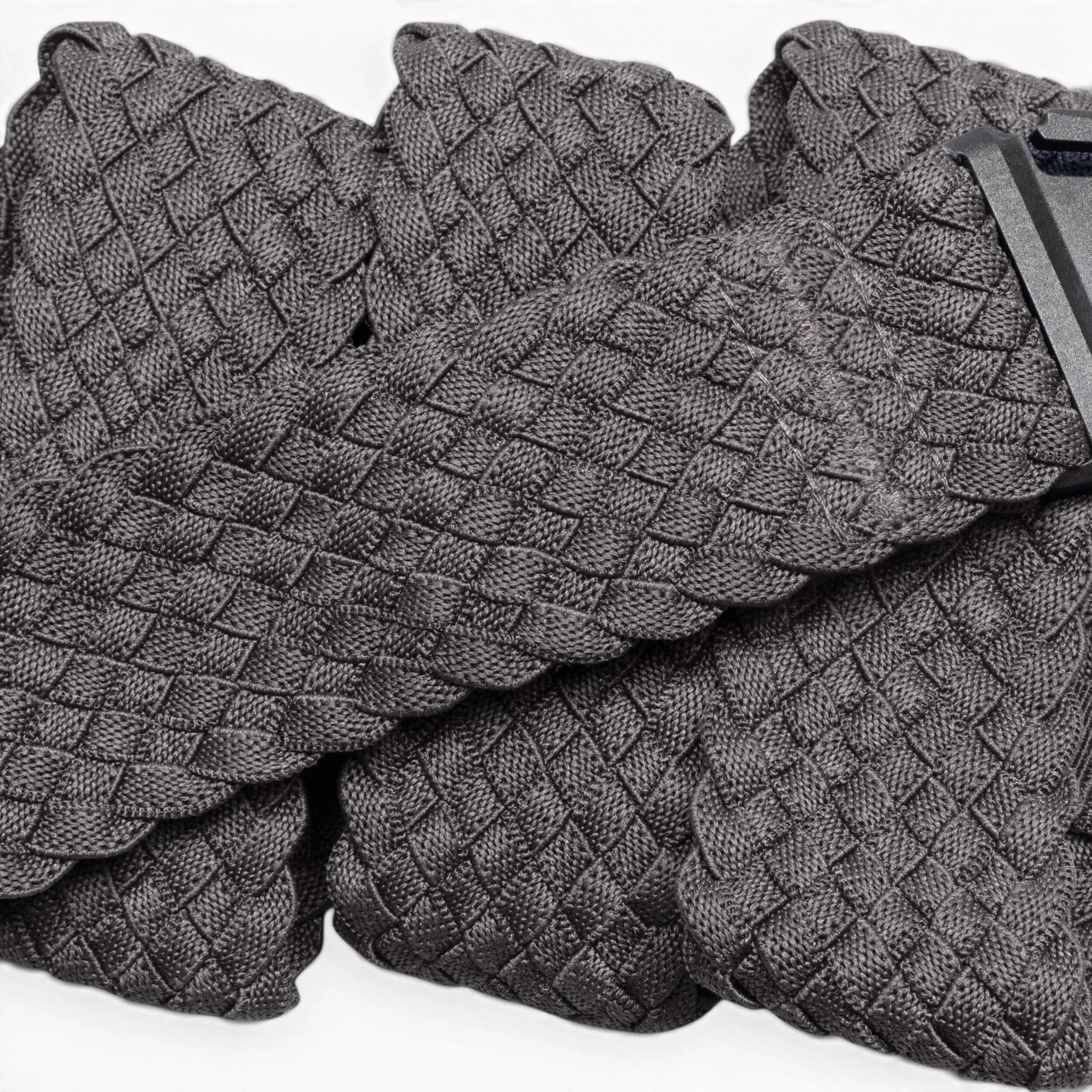 A close-up of Futureweave by Arcade Belts shows its textured gray basketweave fabric, featuring folded sections and a partially visible clothing tag in the top right corner.