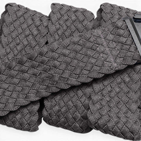 A close-up of Futureweave by Arcade Belts shows its textured gray basketweave fabric, featuring folded sections and a partially visible clothing tag in the top right corner.
