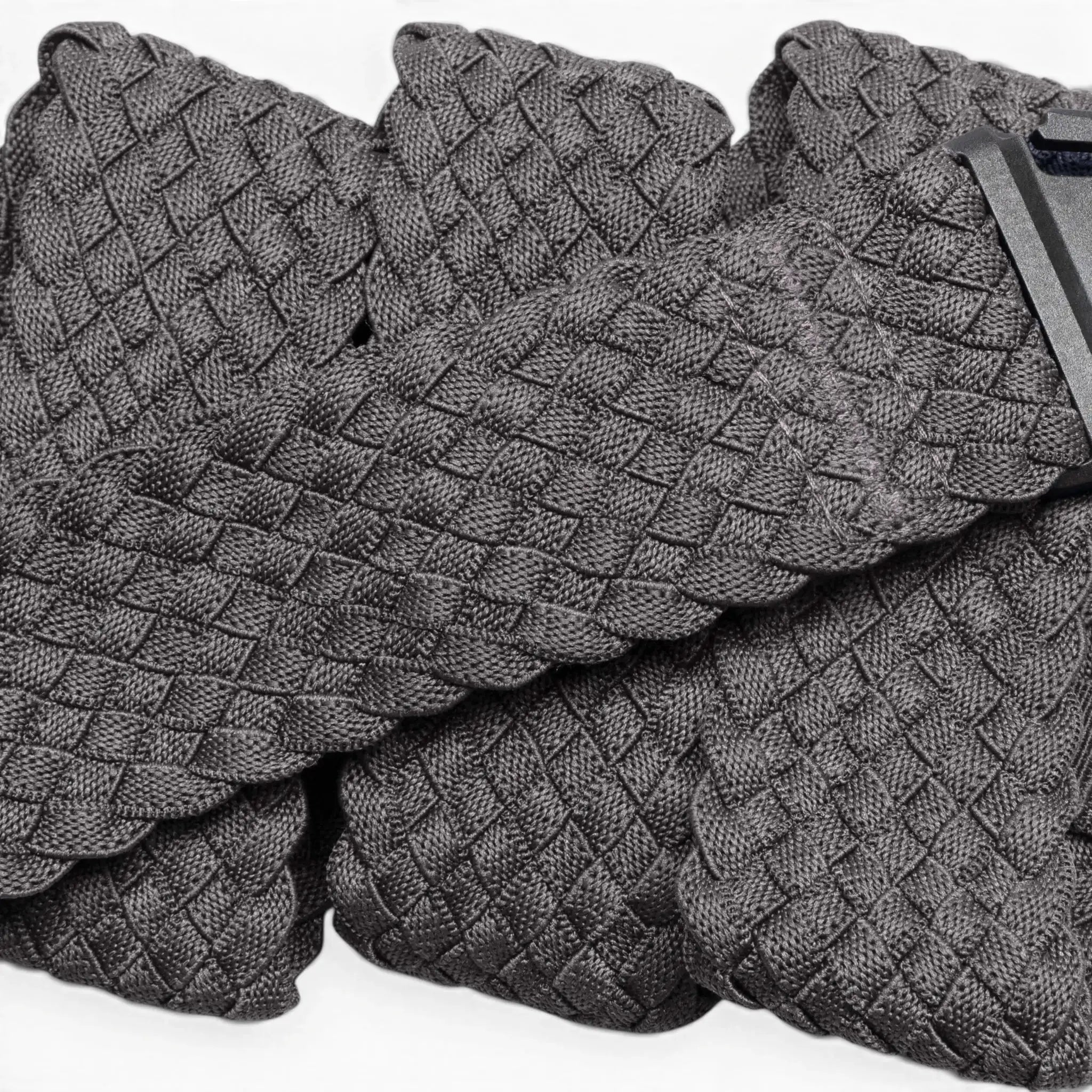 A close-up of Futureweave by Arcade Belts shows its textured gray basketweave fabric, featuring folded sections and a partially visible clothing tag in the top right corner.