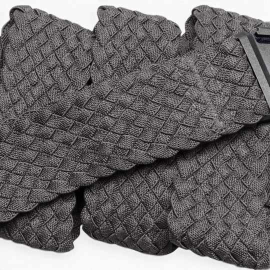 A close-up of Futureweave by Arcade Belts shows its textured gray basketweave fabric, featuring folded sections and a partially visible clothing tag in the top right corner.