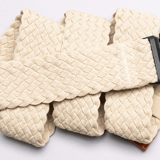A close-up of the Arcade Belts Futureweave, a beige braided travel belt with a dark metal buckle, shown in overlapping folds on a light background.