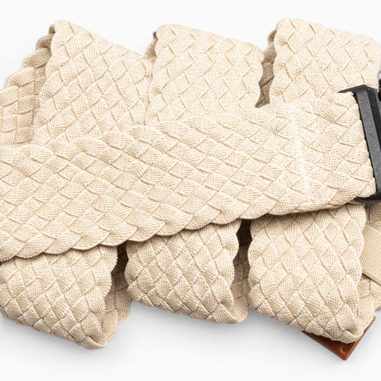 A close-up of the Arcade Belts Futureweave, a beige braided travel belt with a dark metal buckle, shown in overlapping folds on a light background.