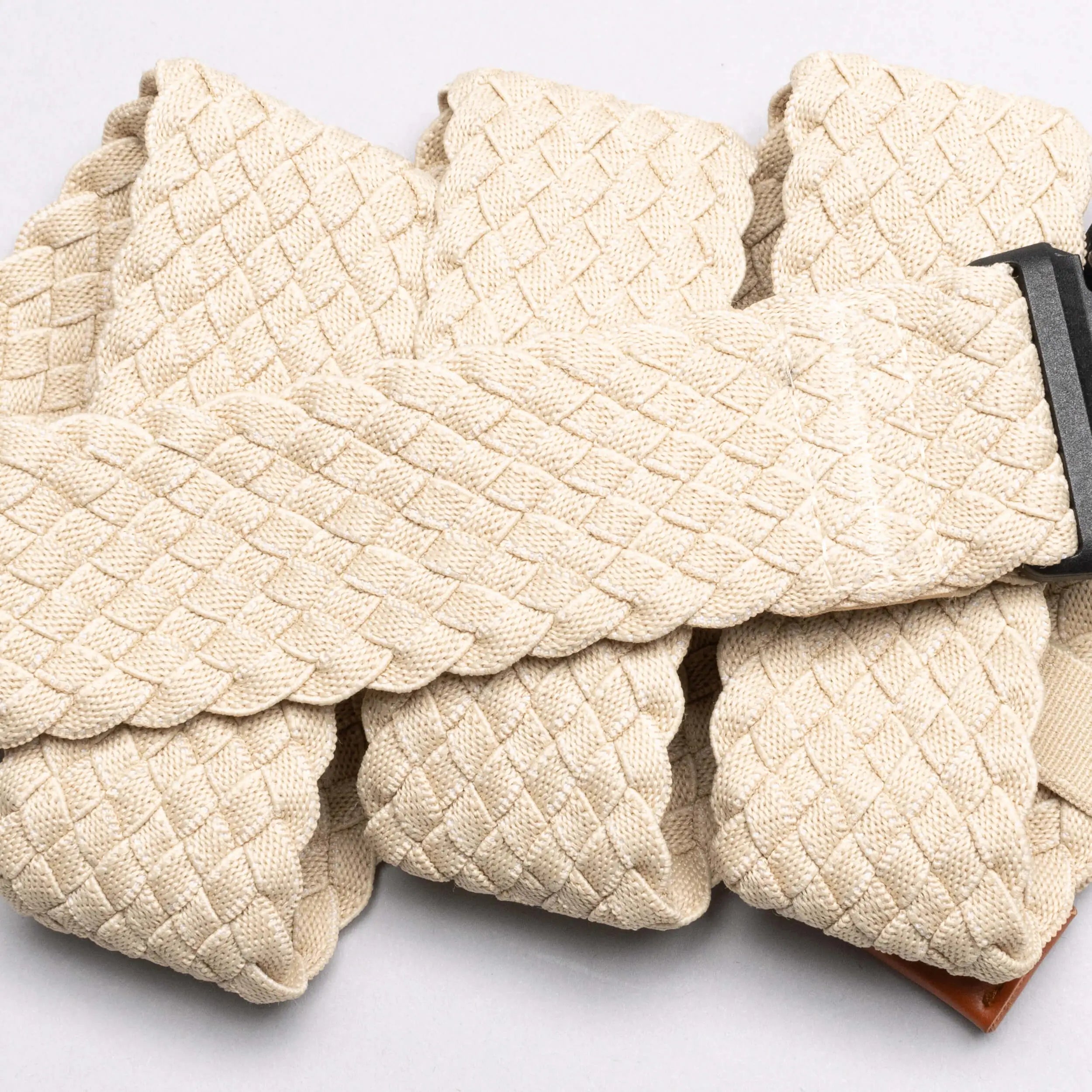 A close-up of the Arcade Belts Futureweave, a beige braided travel belt with a dark metal buckle, shown in overlapping folds on a light background.