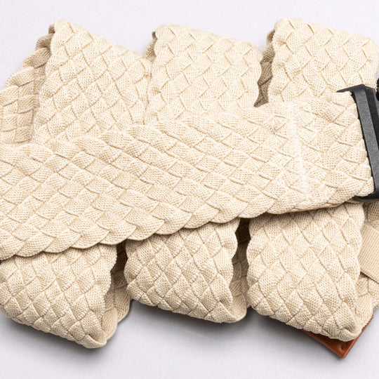 A close-up of the Arcade Belts Futureweave, a beige braided travel belt with a dark metal buckle, shown in overlapping folds on a light background.