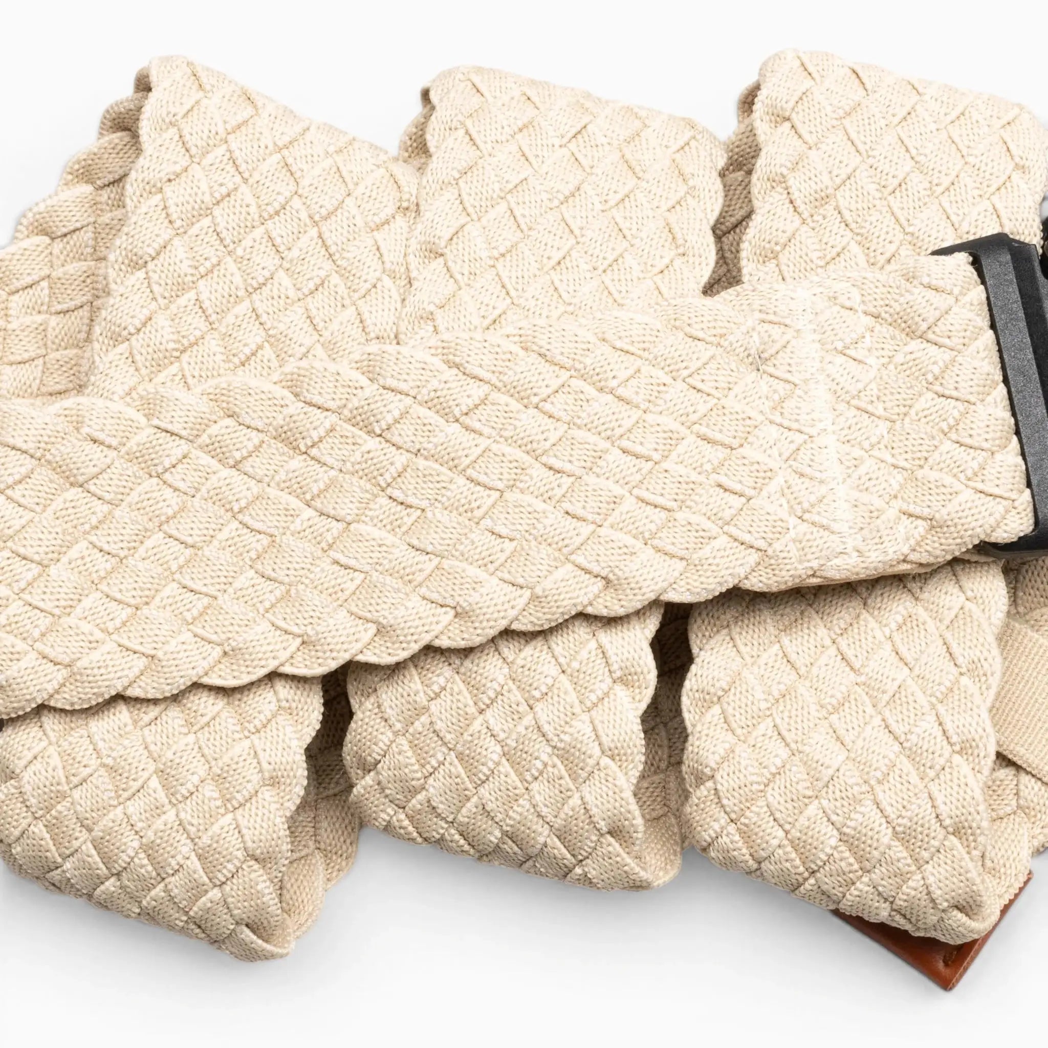 A close-up of the Arcade Belts Futureweave, a beige braided travel belt with a dark metal buckle, shown in overlapping folds on a light background.