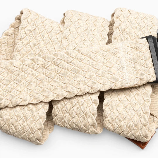 A close-up of the Arcade Belts Futureweave, a beige braided travel belt with a dark metal buckle, shown in overlapping folds on a light background.