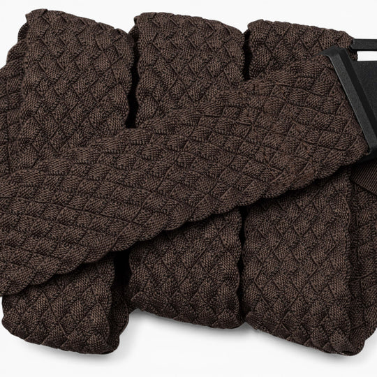A close-up of the Arcade Belts Futureweave, a textured dark brown belt with a geometric diamond pattern, crafted from lightweight woven webbing for all-day comfort and featuring a partially visible rectangular black metal buckle.
