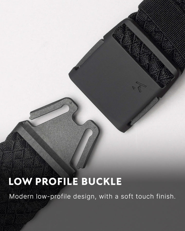 Close-up of a low profile belt with a modern, matte buckle and textured stretch webbing strap. Text on the image reads: Low Profile Buckle. Perfect for travel belts, featuring a soft touch finish and sleek, modern design.