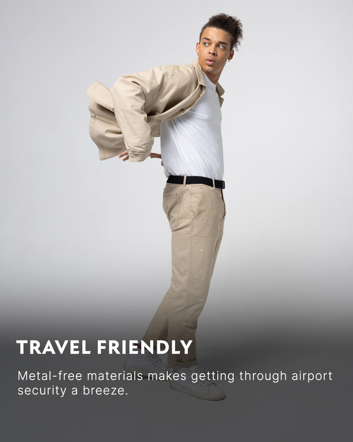 A person in a light-colored jacket, white t-shirt, and beige pants stands in a dynamic pose. Text reads: TRAVEL FRIENDLY. Arcade Belts with plastic buckle and elastic stretch belt make airport security a breeze.