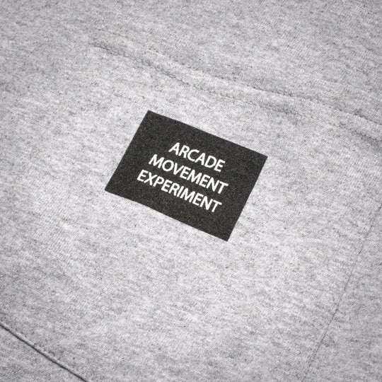 A close-up of the Arcade Movement Experiment Tee by Arcade Belts, showcasing gray fabric and a black patch with ARCADE MOVEMENT EXPERIMENT.