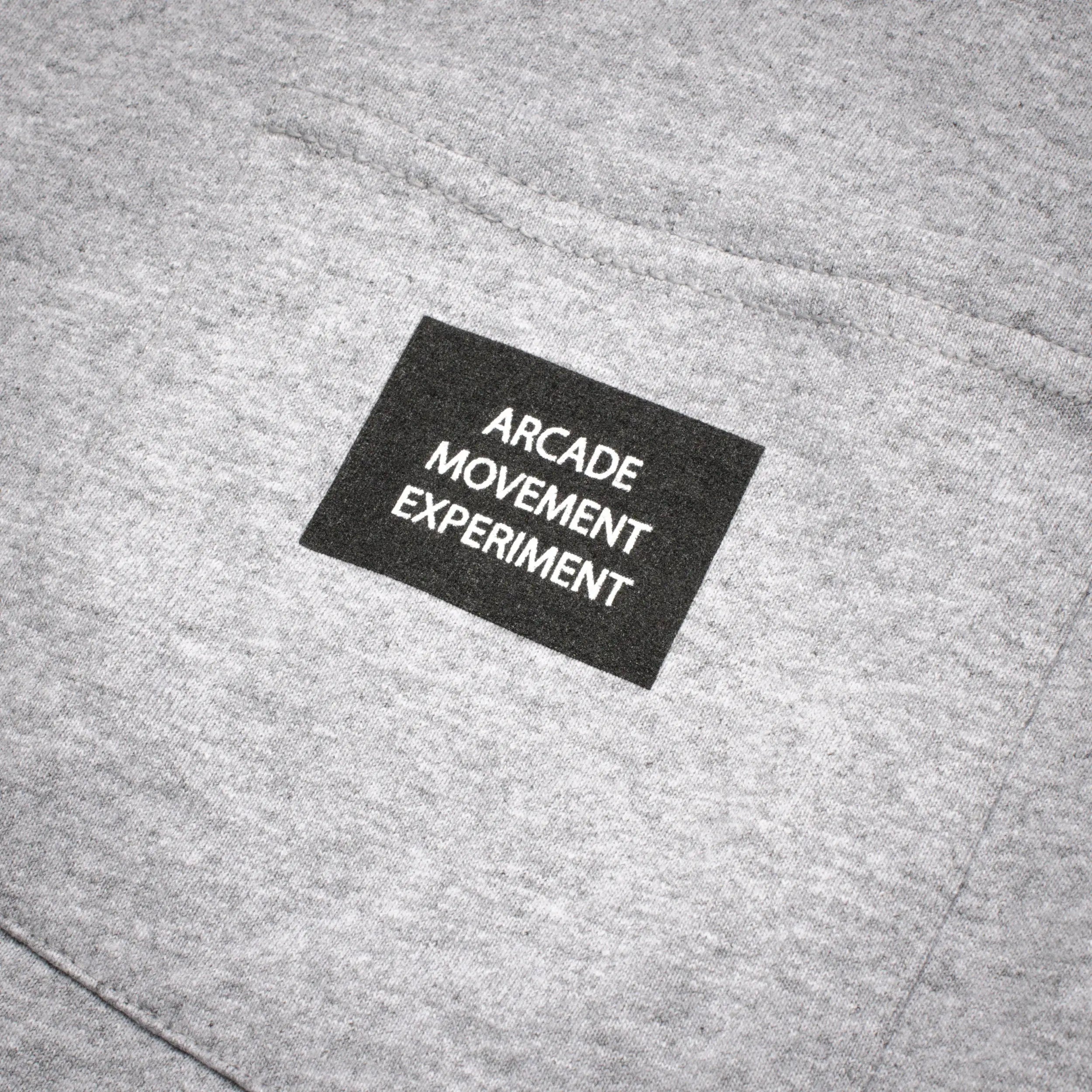A close-up of the Arcade Movement Experiment Tee by Arcade Belts, showcasing gray fabric and a black patch with ARCADE MOVEMENT EXPERIMENT.