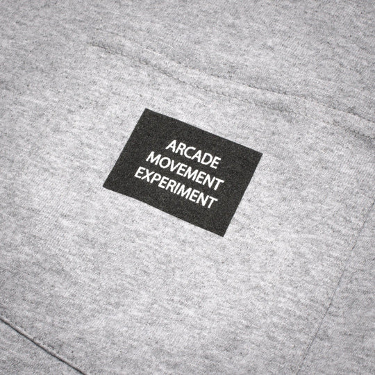 A close-up of the Arcade Movement Experiment Tee by Arcade Belts, showcasing gray fabric and a black patch with ARCADE MOVEMENT EXPERIMENT.