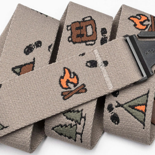 A close-up of the Get Outside hiking belt by Arcade Belts in beige, embroidered with camping icons like a campfire, tent, pine tree, backpack, and footprints. The black buckle is partially visible—a top pick for outdoor lovers.