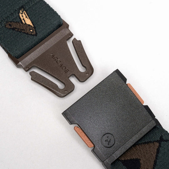 Close-up of the Get Outside belt by Arcade Belts: a dark green elastic stretch belt with a metal buckle engraved ARCADE and a stylized bird on the strap. The low-profile design pops against the white background.