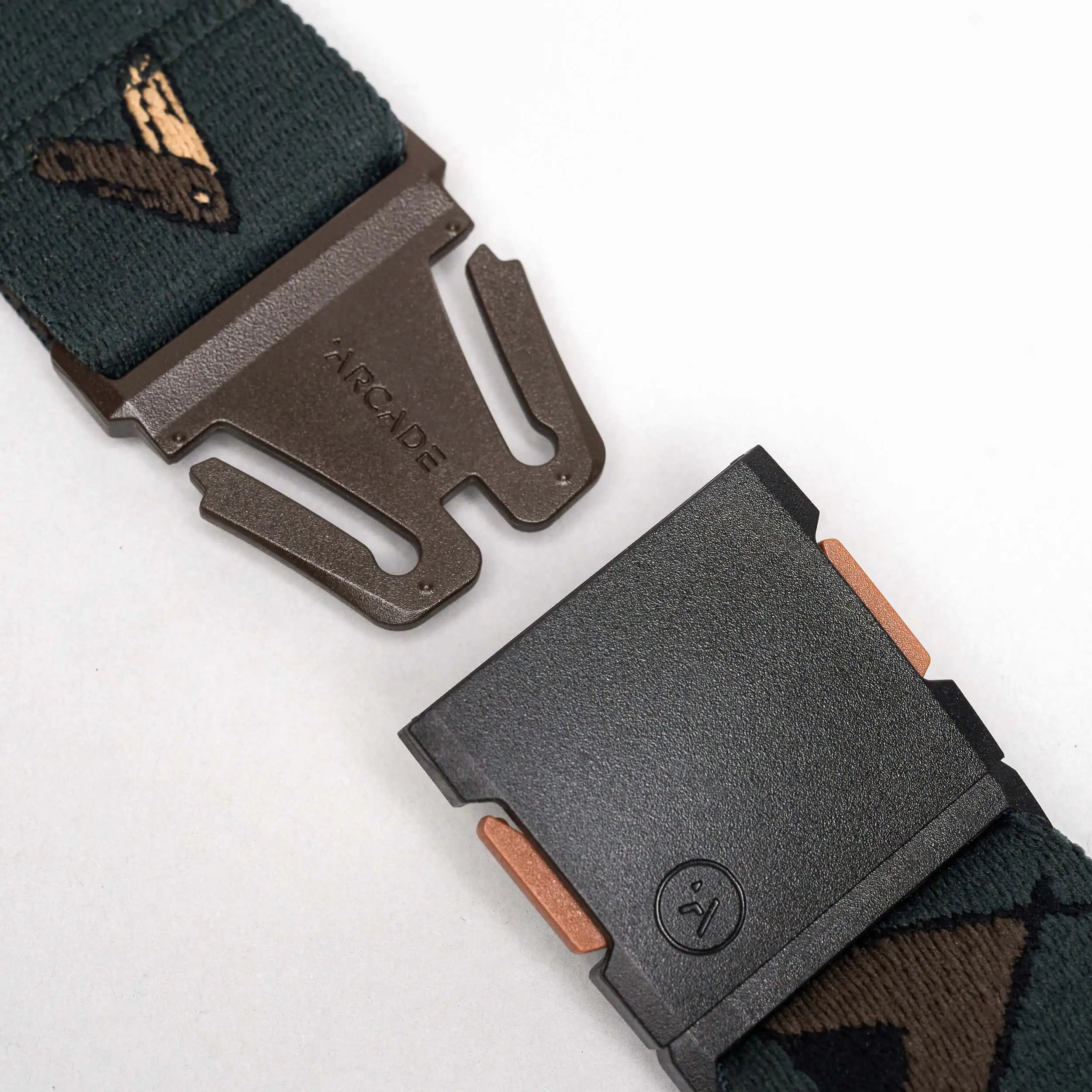 Close-up of the Get Outside belt by Arcade Belts: a dark green elastic stretch belt with a metal buckle engraved ARCADE and a stylized bird on the strap. The low-profile design pops against the white background.
