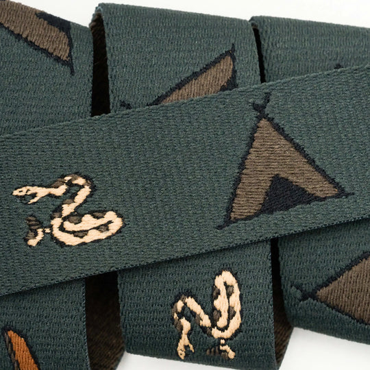 The Get Outside ribbon from Arcade Belts features green woven fabric with beige snakes and brown teepees, similar to Low Profile Belt designs. The ribbon is partially folded, creating overlapping layers.