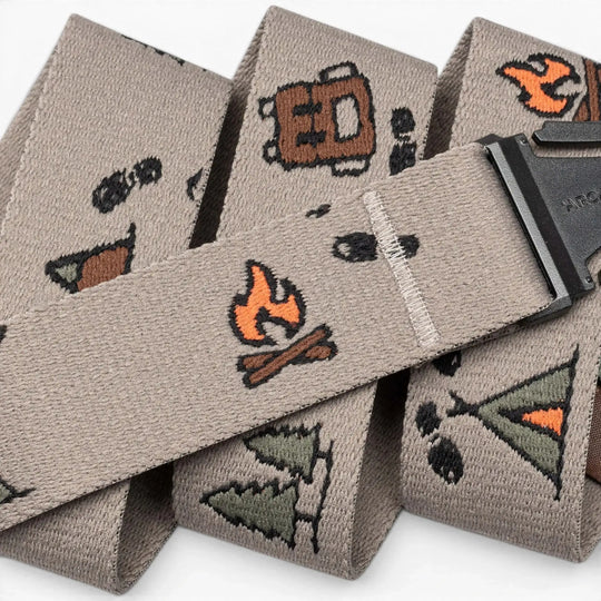 A close-up of the Get Outside hiking belt by Arcade Belts in beige, embroidered with camping icons like a campfire, tent, pine tree, backpack, and footprints. The black buckle is partially visible—a top pick for outdoor lovers.